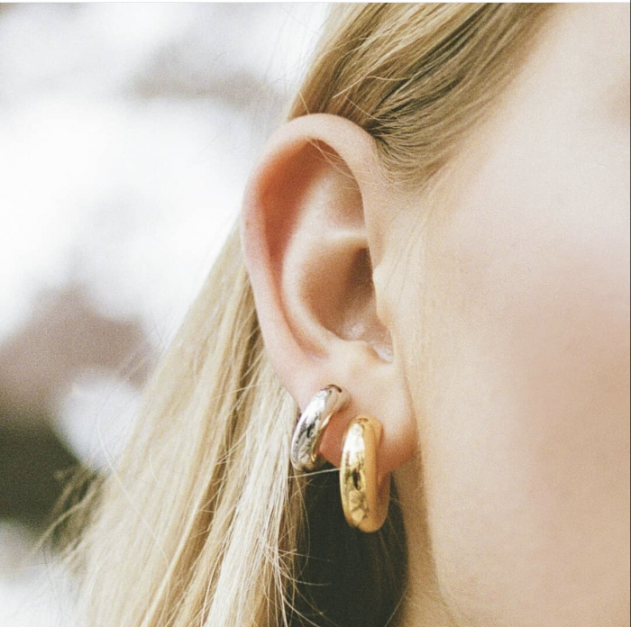 White woman's ear with silver and gold hoop earrings.