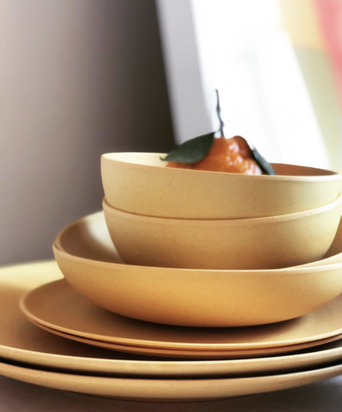 stack of yellow fable dishware with single orange resting in top bowl