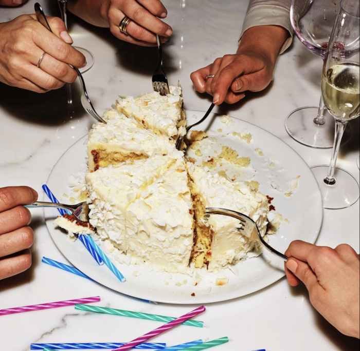 group of hands holding forks and digging into birthday cake