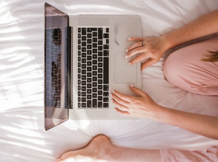 woman sitting on bed working from mac computer