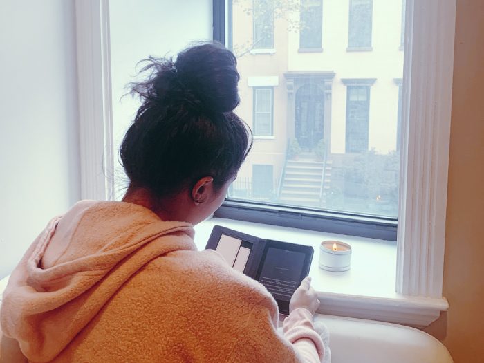 NYU student reading by window in NYC apartment with candle lit